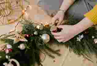 A woman's hands place ornaments into a beautiful christmas wreath