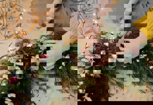 A woman's hands place ornaments into a beautiful christmas wreath