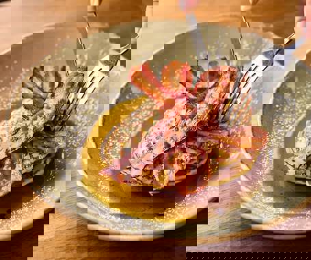 A knife and fork cutting into a stack on pancakes topped with streaky bacon and maple syrup