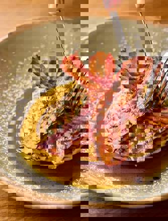 A knife and fork cutting into a stack on pancakes topped with streaky bacon and maple syrup