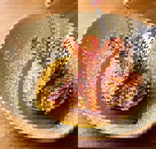 A knife and fork cutting into a stack on pancakes topped with streaky bacon and maple syrup