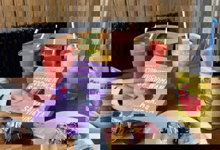 A hand holding a book with a delicious slice of cake and a selection of ice cold drinks on the table