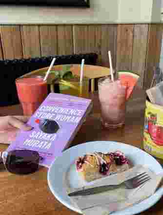 A hand holding a book with a delicious slice of cake and a selection of ice cold drinks on the table