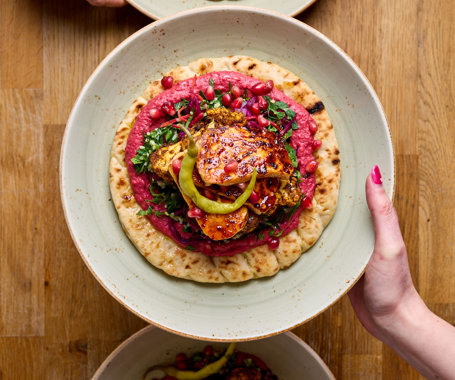 Three hands holding three plates containing our brand new Cauliflower Shawarma with Flatbread of as a Buddha Bowl. Two diesh also contain Hot Honey Halloumi