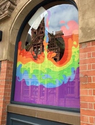 A window with beautiful pride artwork with a jug pouring the pride colours like a liquid.