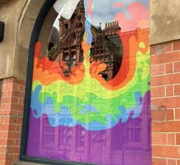 A window with beautiful pride artwork with a jug pouring the pride colours like a liquid.