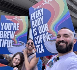 3 people hold large signs with messages supporting the LGBTQ+ community