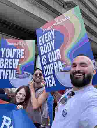 3 people hold large signs with messages supporting the LGBTQ+ community