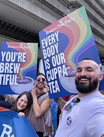 3 people hold large signs with messages supporting the LGBTQ+ community