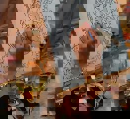 A woman's had paints an angel onto a canvas with a glass of wine nearby