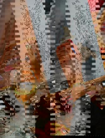 A woman's had paints an angel onto a canvas with a glass of wine nearby