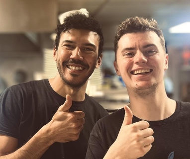 Two males giving their thumbs up to the camera and smiling