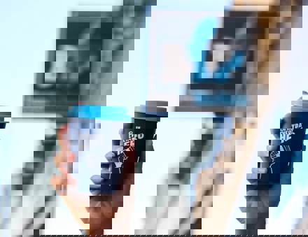 A hand holding a blue reusable coffee cup with the words 'Be an everyday hero' in white written across it