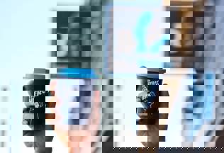 A hand holding a blue reusable coffee cup with the words 'Be an everyday hero' in white written across it