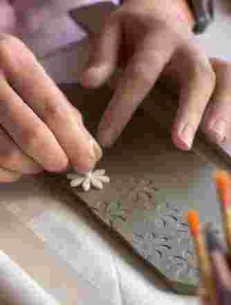 A hand gently stencils a flower pattern into soft clay