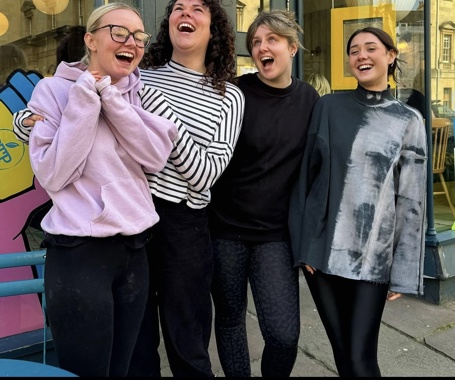 Four women who work for Boston, arms around one another, smiling and laughing